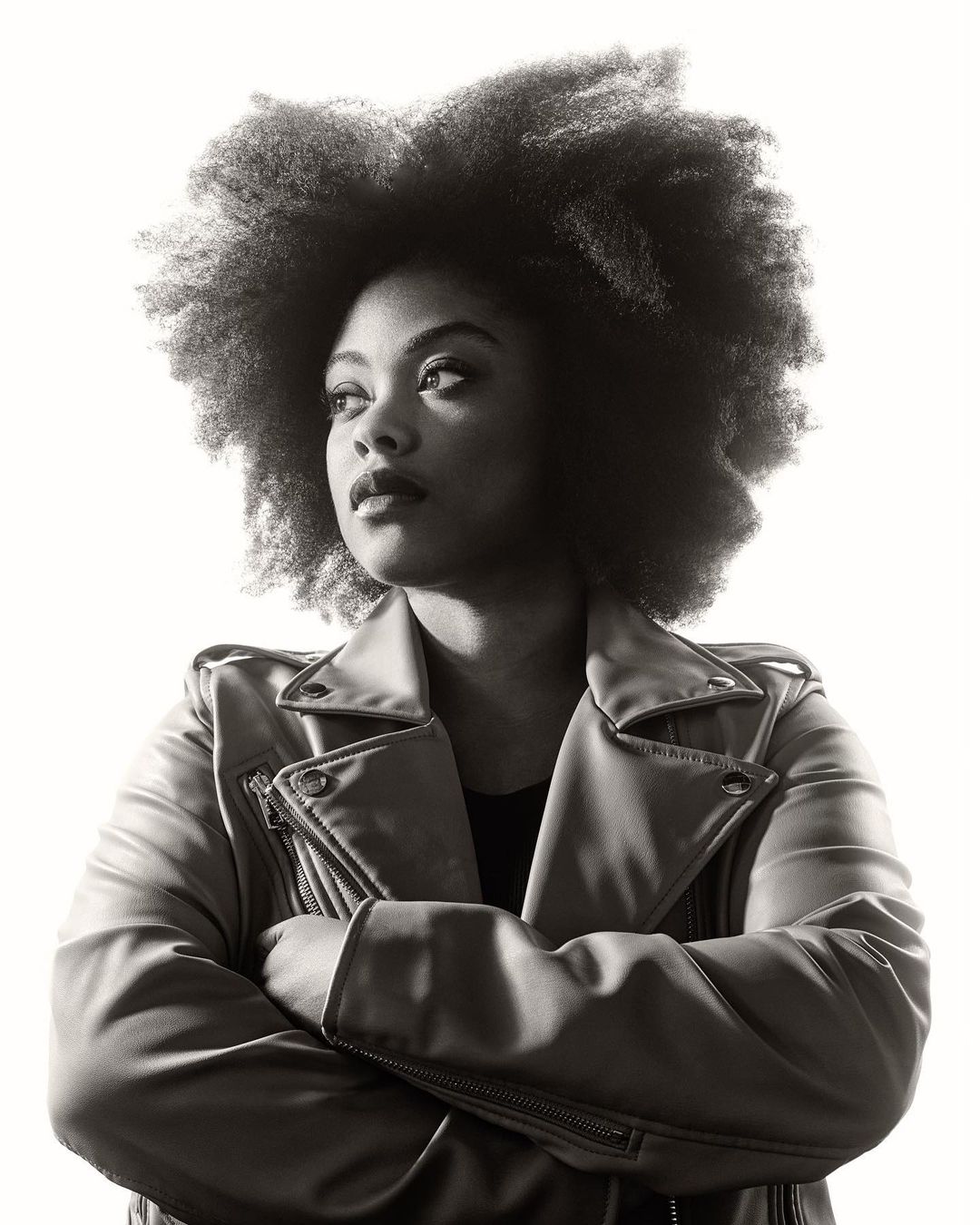 Portrait of a Black woman with an afro wearing a leather jacket with arms crossed, photographed by Kremer Johnson.